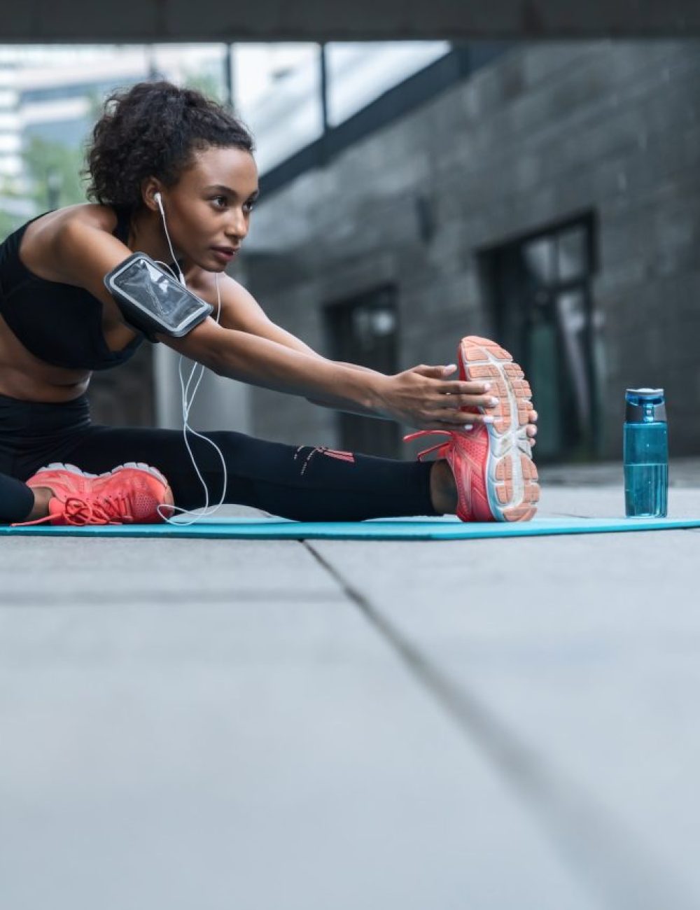 Fitness woman with earphones exercising and stretching outdoors on fitness mat